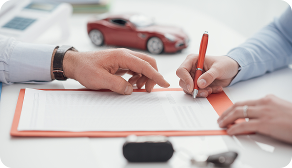 Два человека подписывают договор за столом, на котором лежат ключи и модель красного автомобиля.