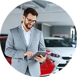 Мужчина в костюме смотрит на планшет, стоя рядом с красным автомобилем.